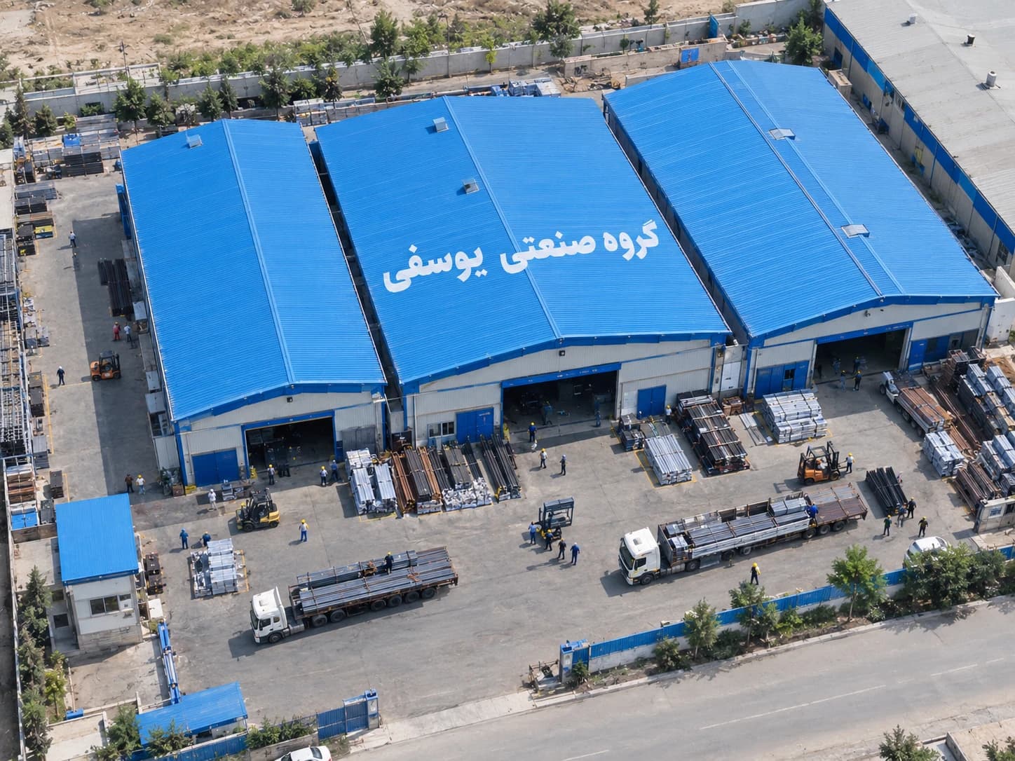 نمای هوایی کارخانه گروه صنعتی یوسفی با سولههای آبی، کامیونهای حمل پروفیل و محوطه بارگیری